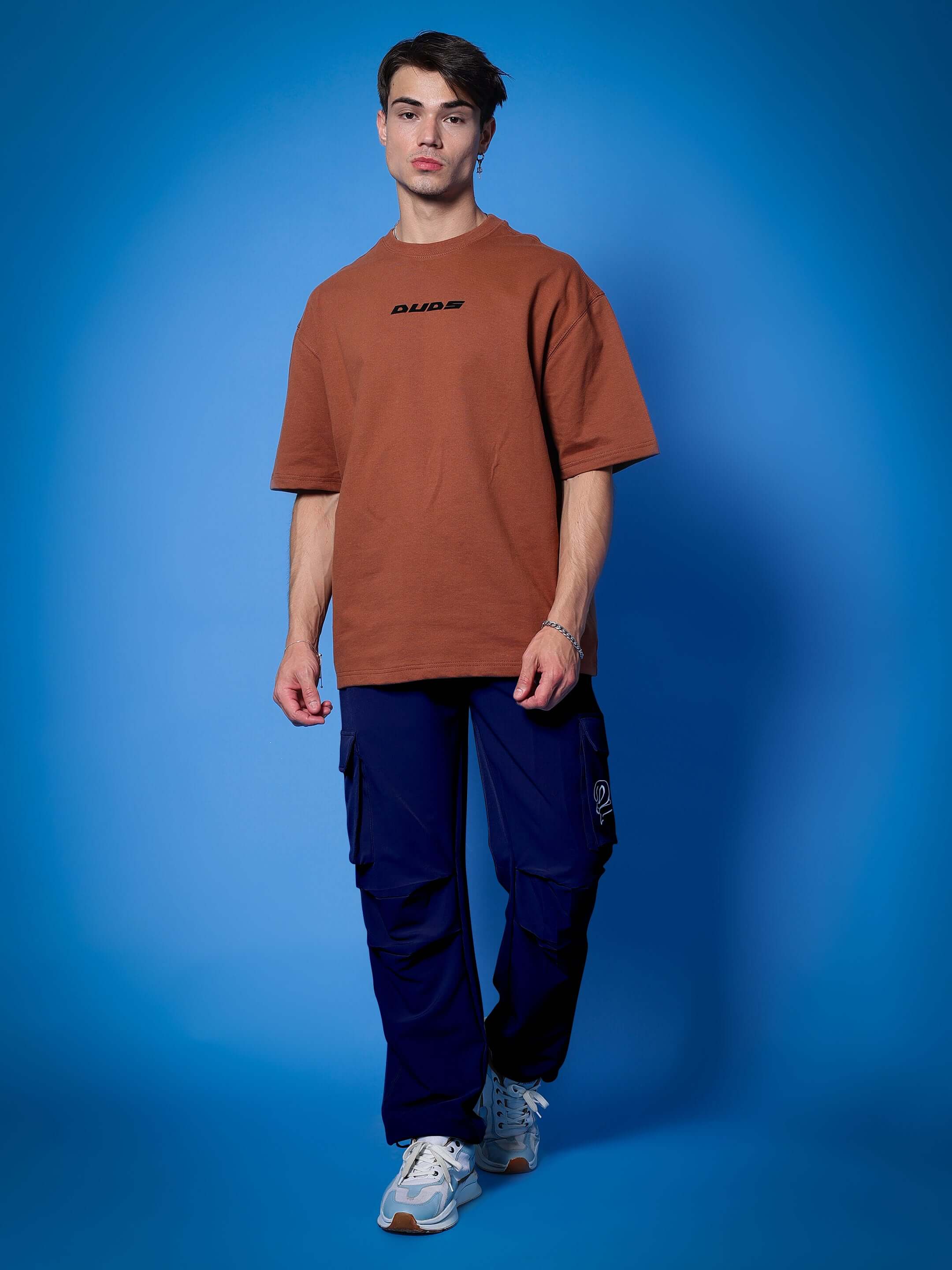 Model wearing MYRIAD RELAXED FIT CARGO PANTS NAVY BLUE with brown shirt against blue background