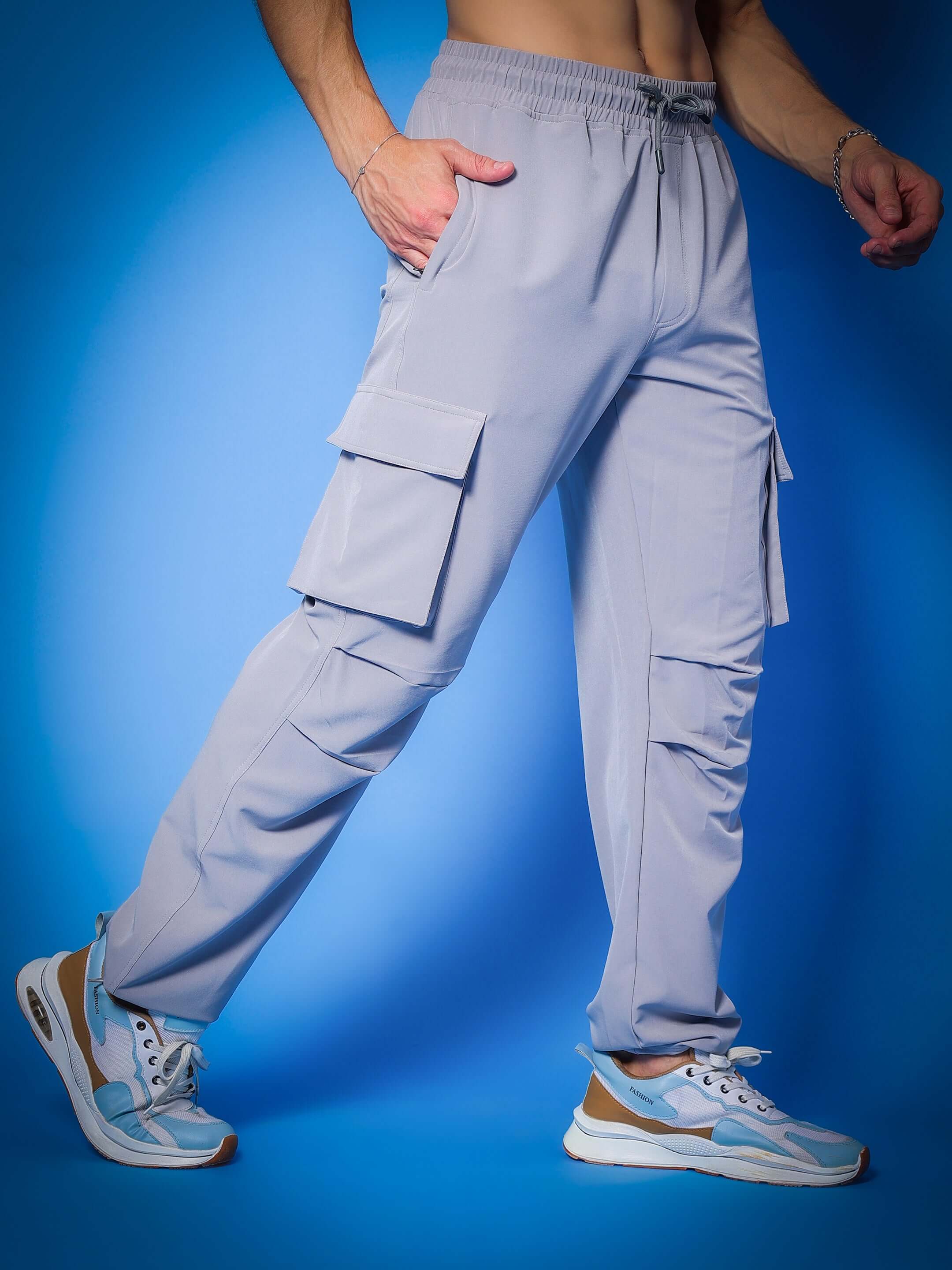 Model wearing MYRIAD relaxed fit grey cargo pants with pockets, showcasing casual style on a blue background.