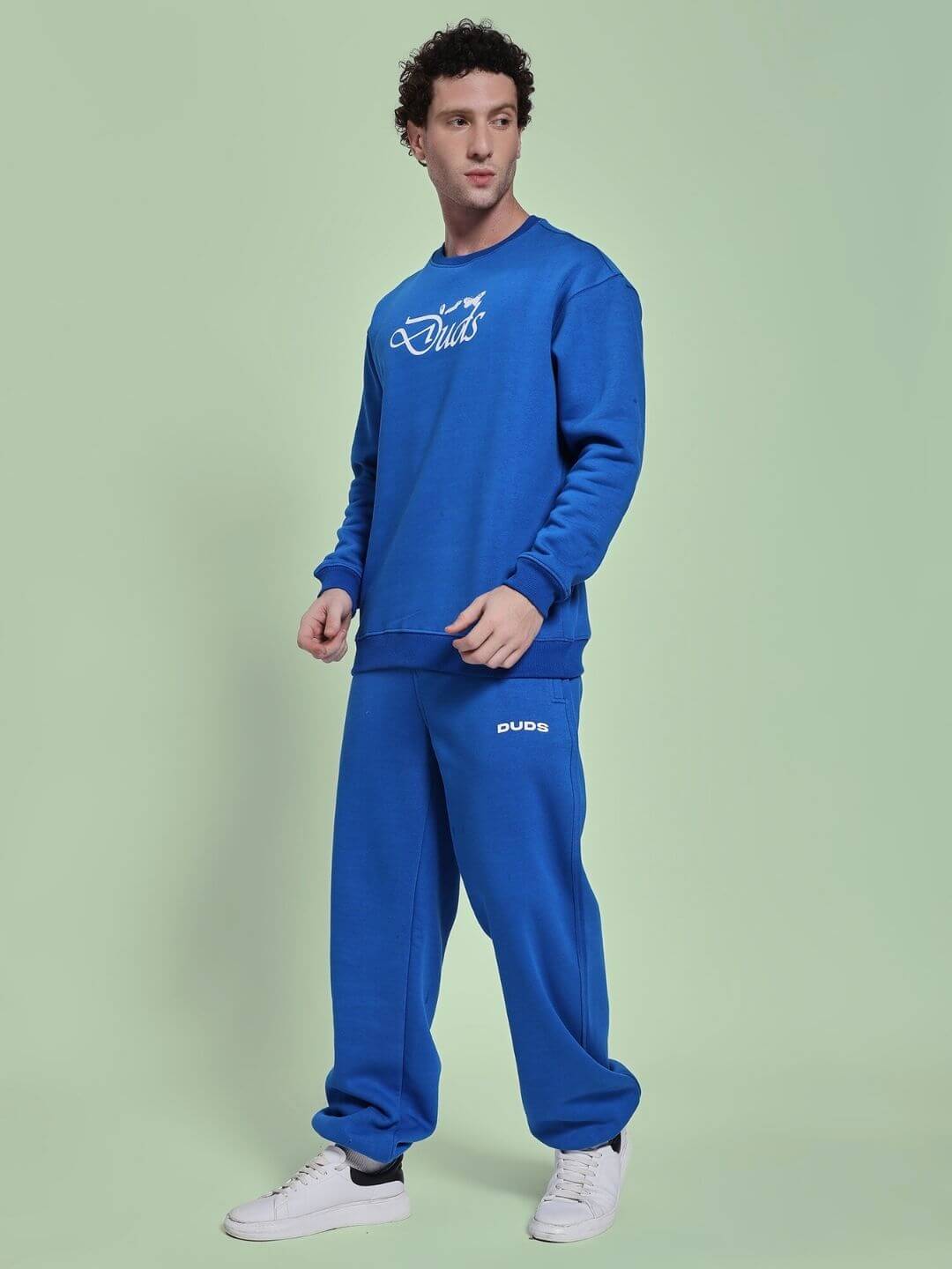 Man wearing NATURE LINK FLEECE CO-ORD SET ROYAL BLUE featuring sweatshirt and joggers against green background.