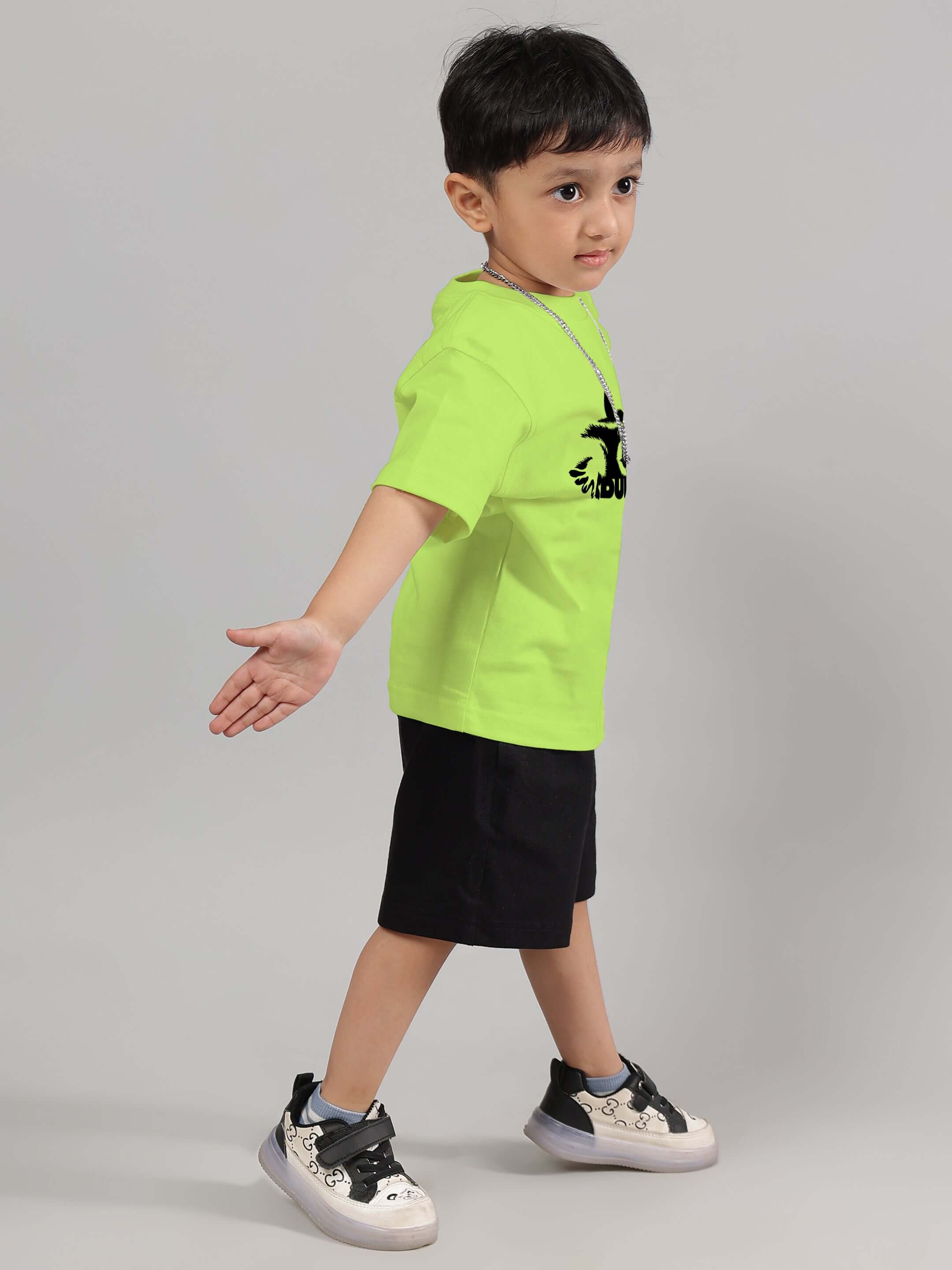 Child wearing neon green raccoon t-shirt, black shorts, and sneakers, posing against a neutral background.