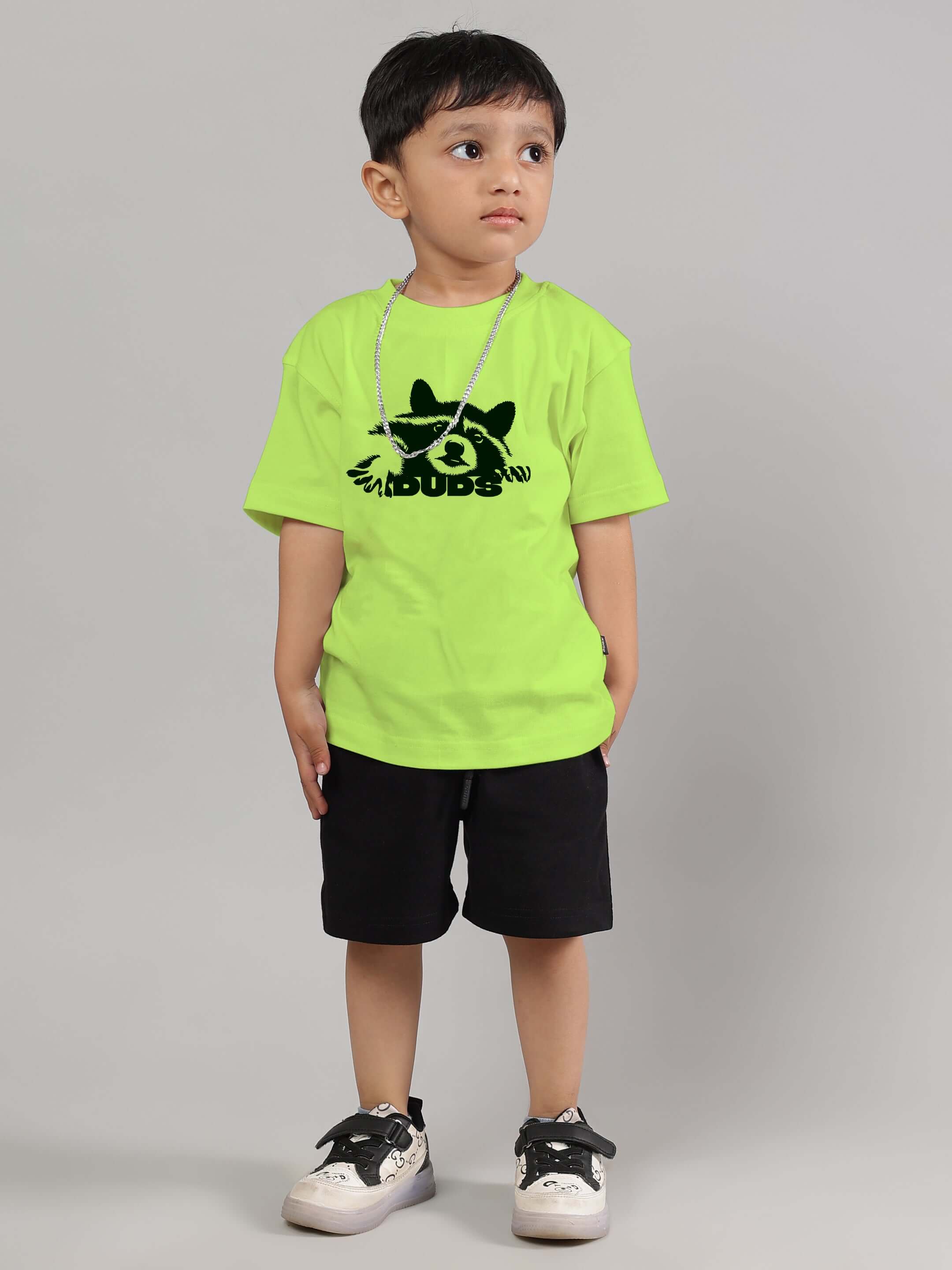 Boy wearing neon green raccoon t-shirt for boys and girls, paired with black shorts and sneakers, from DUDS collection.
