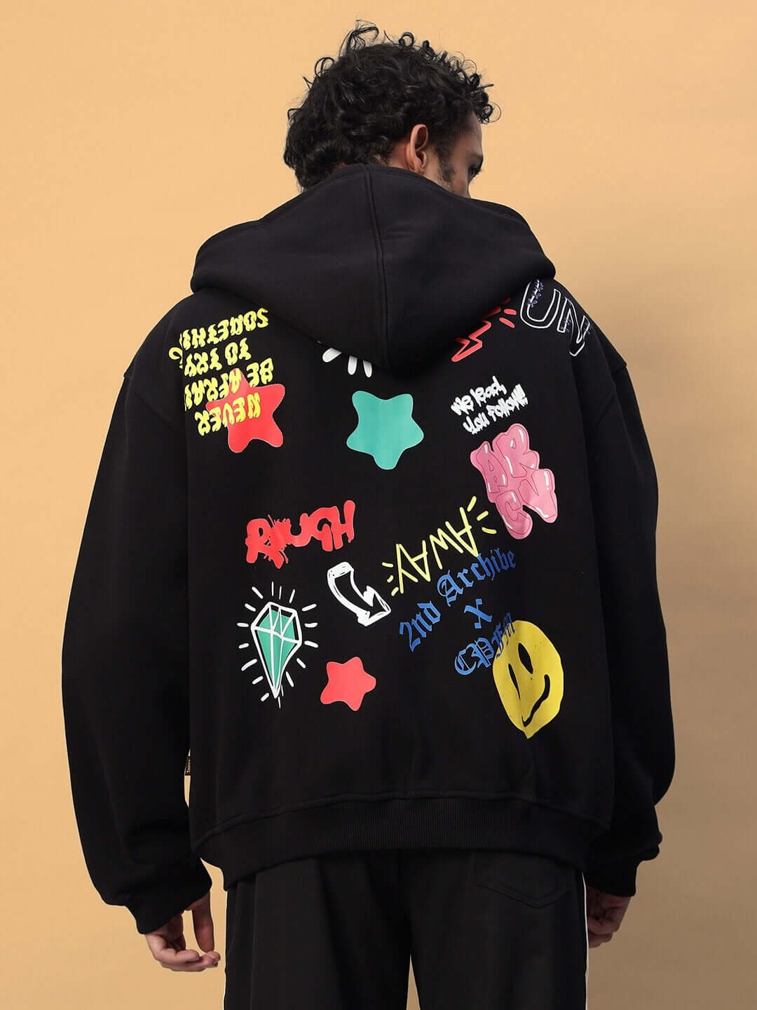 Man wearing NEVER BE AFRAID FLEECE HOODIE BLACK with colorful graphic designs on the back.