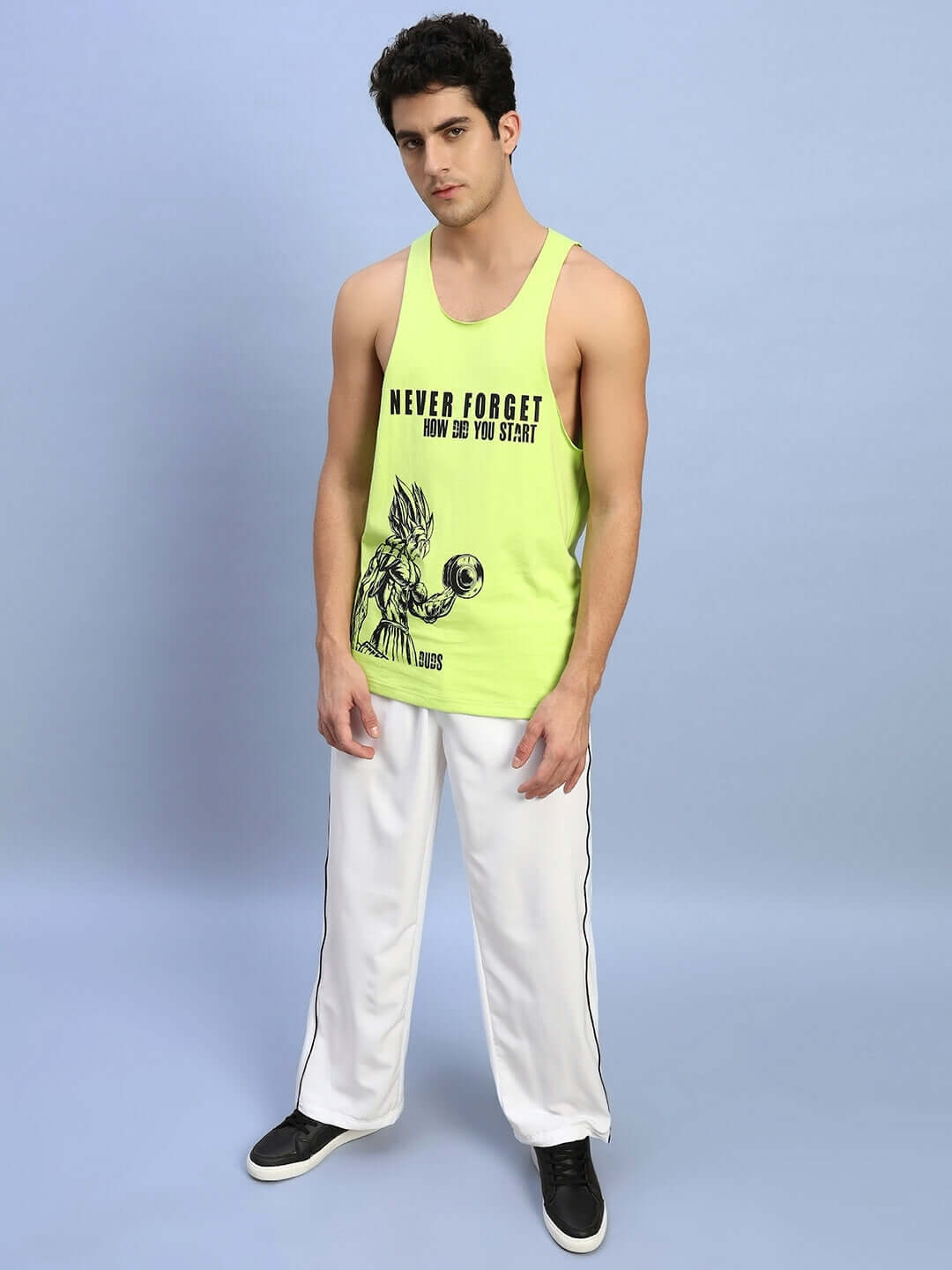 Man wearing neon green 'Never Forget' printed gym t-shirt, paired with white pants, standing against a pale blue background.