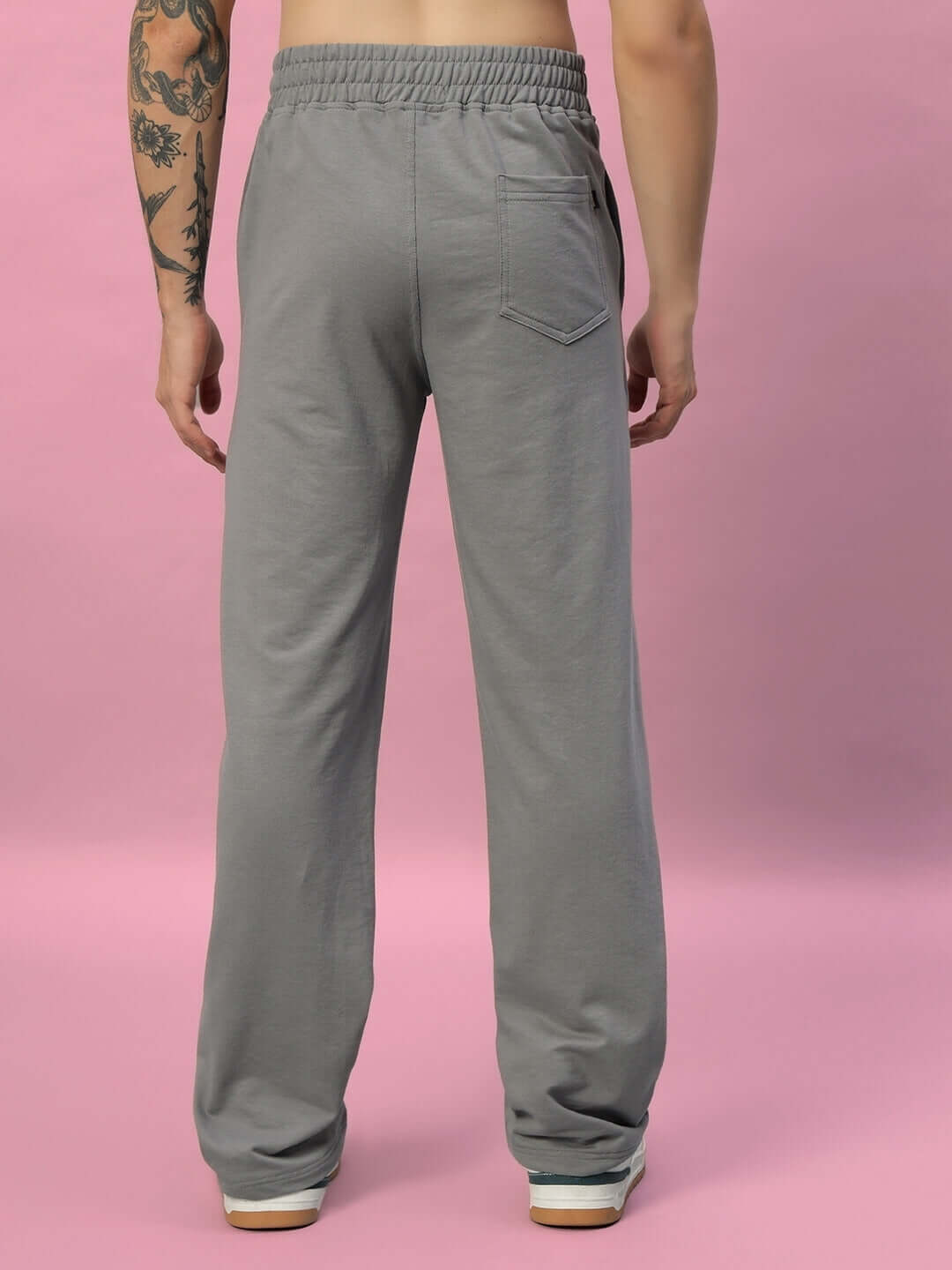 Man wearing New Era Relaxed Fit Joggers in grey, showcasing the rear design against a pink background.
