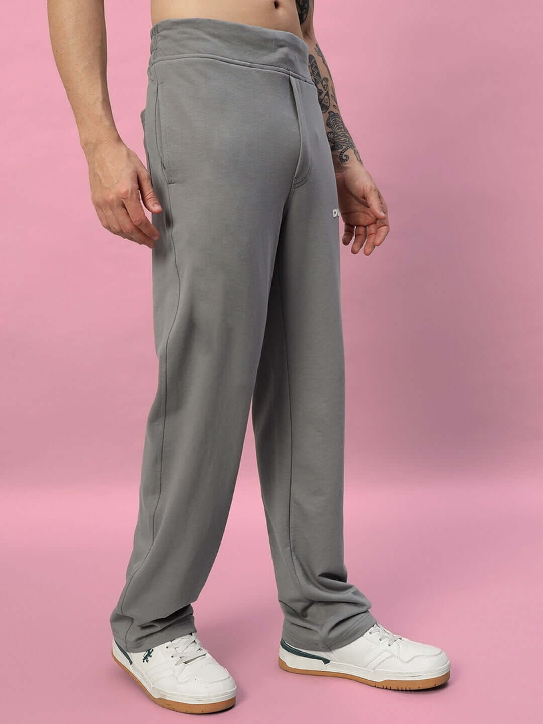 Model wearing NEW ERA Relaxed Fit Joggers in grey, made-to-order with customizable fit option, showcased against a pink background.