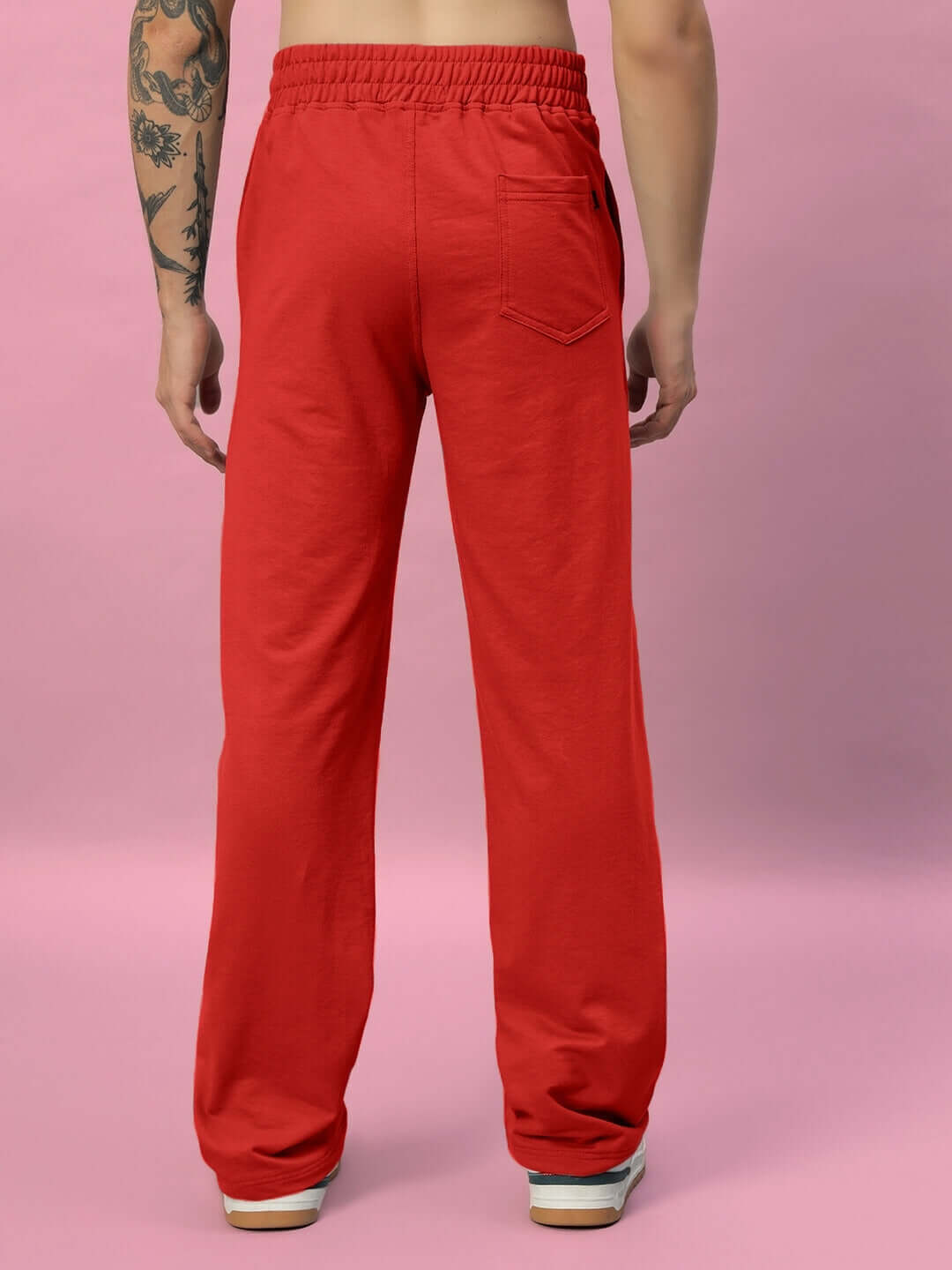 Back view of red New Era relaxed fit joggers with elastic waistband and pocket, worn by model against pink background.