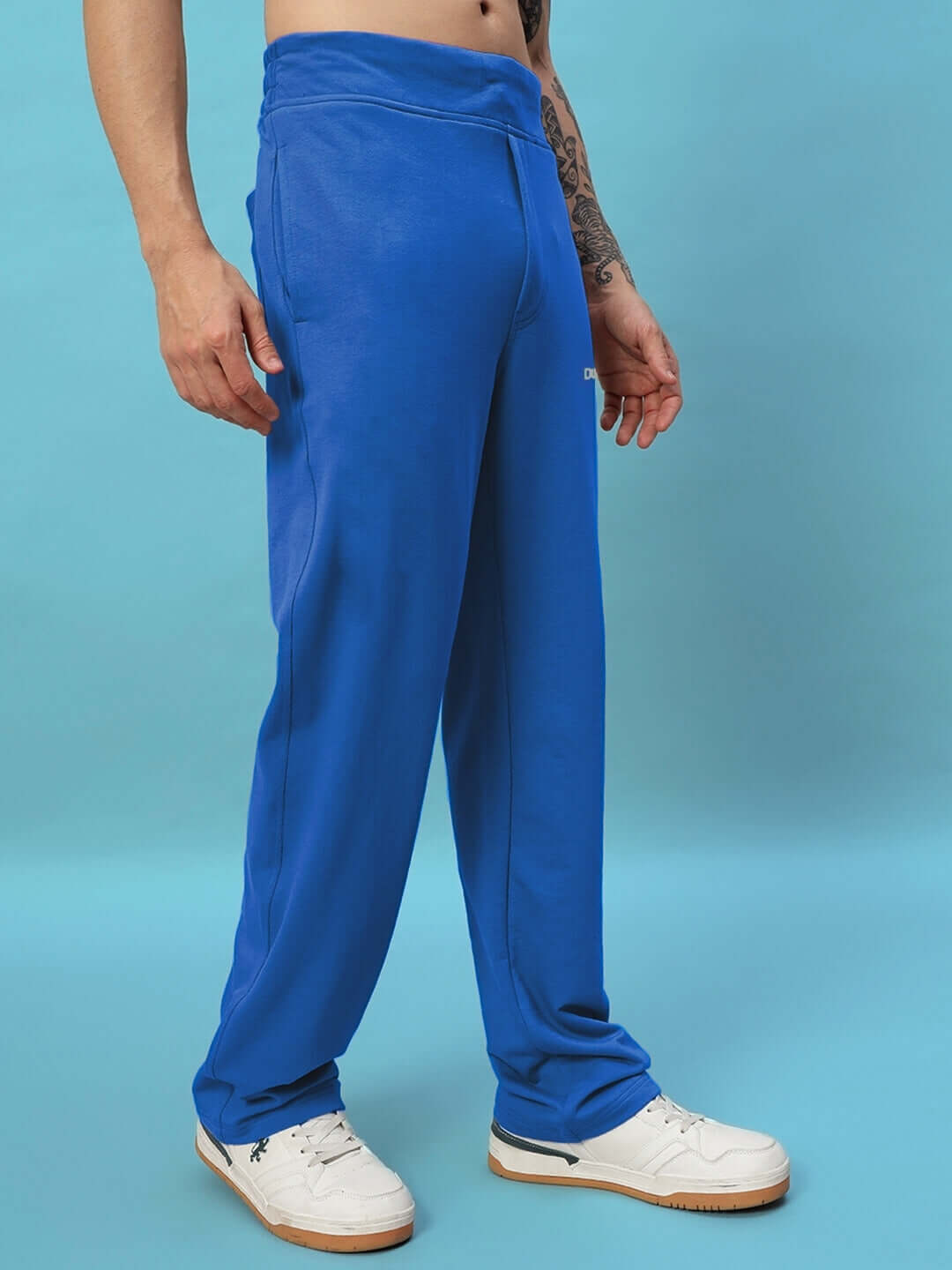 NEW ERA RELAXED FIT JOGGERS ROYAL BLUE showcased on a model wearing white sneakers against a blue background.