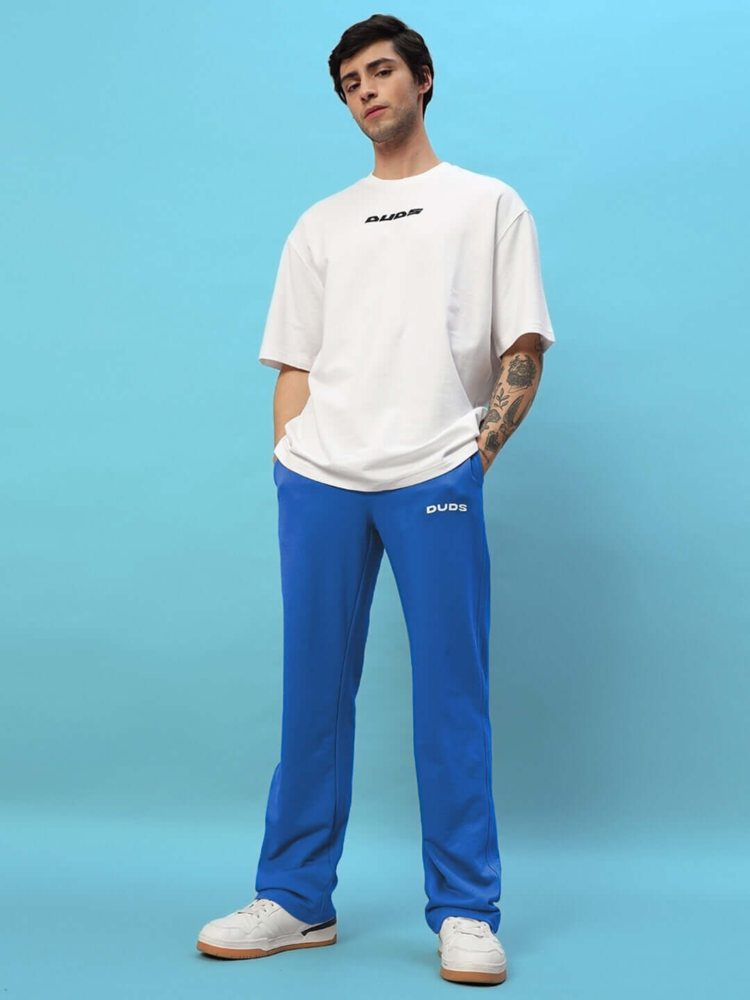 Model wearing New Era Relaxed Fit Joggers Royal Blue with white sneakers and t-shirt, showcasing casual streetwear style.