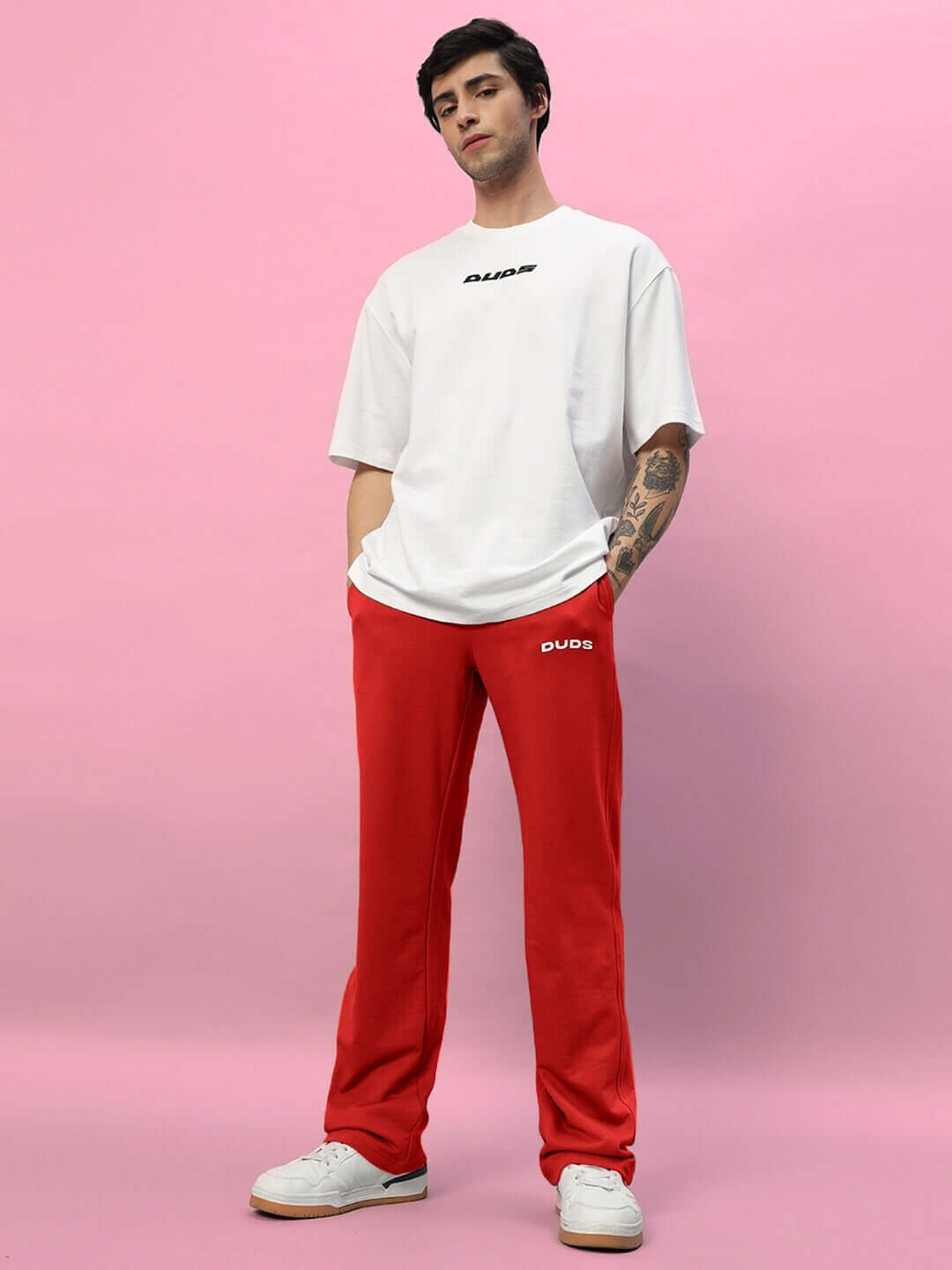 Model wearing New Era Relaxed Fit Red Joggers by DUDS against pink background, showcasing casual style.
