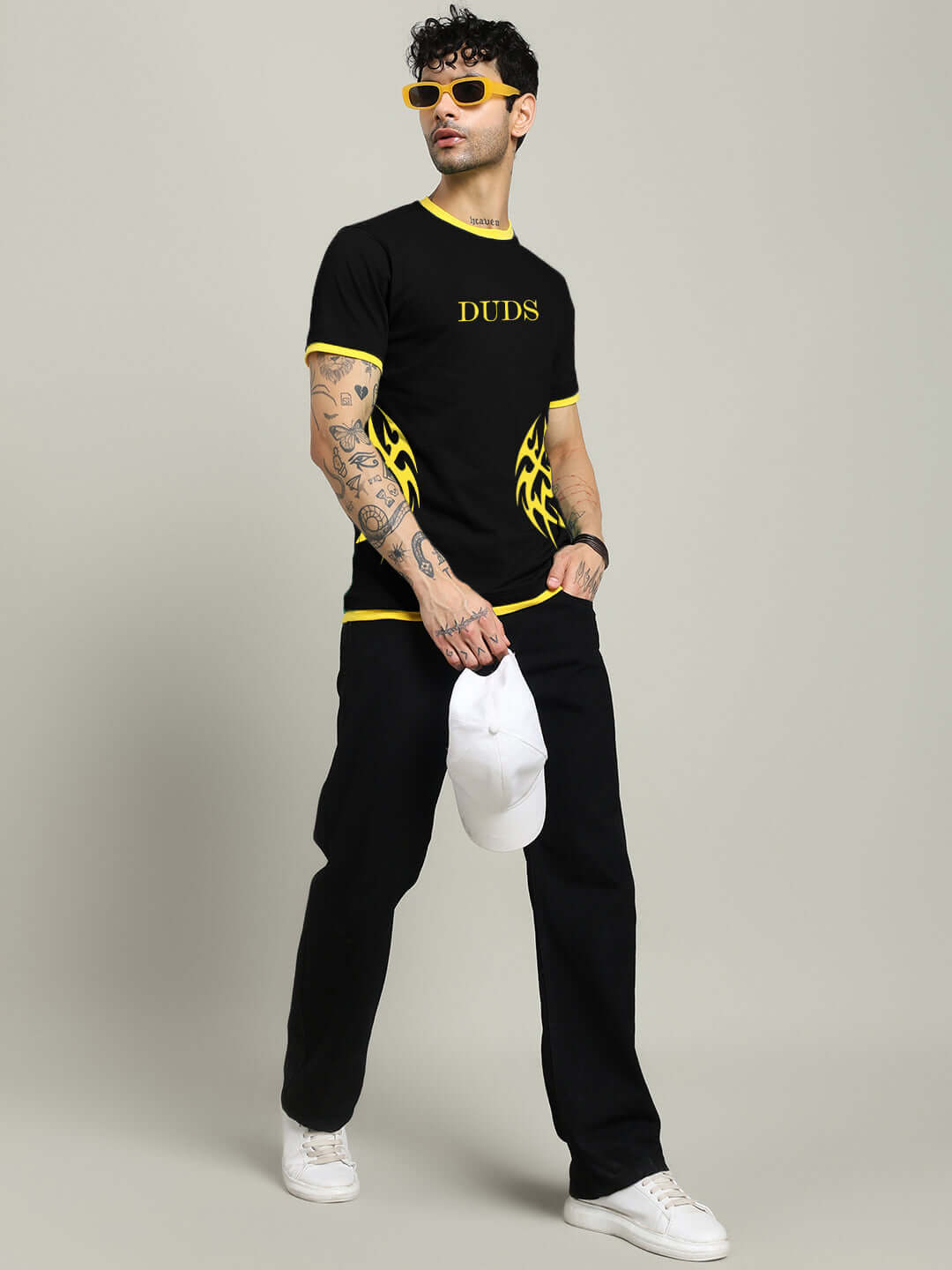 Model wearing NIMO REGULAR FIT T-SHIRT BLACK with yellow details and holding a white cap, showcasing streetwear style.