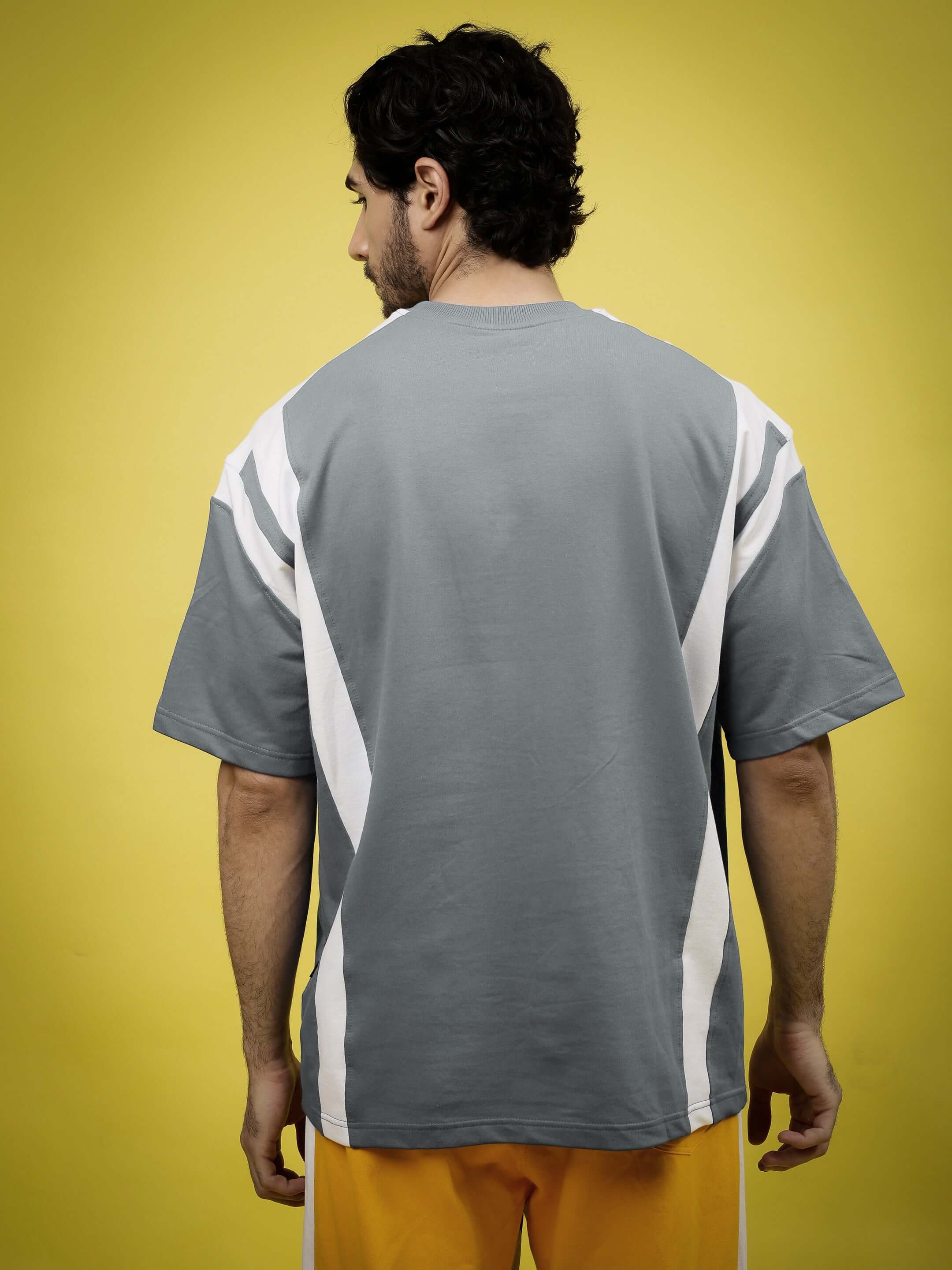 Person wearing NINJA STORM OVER-SIZED T-SHIRT GREY with graphic print, showcasing modern streetwear style against a yellow background.