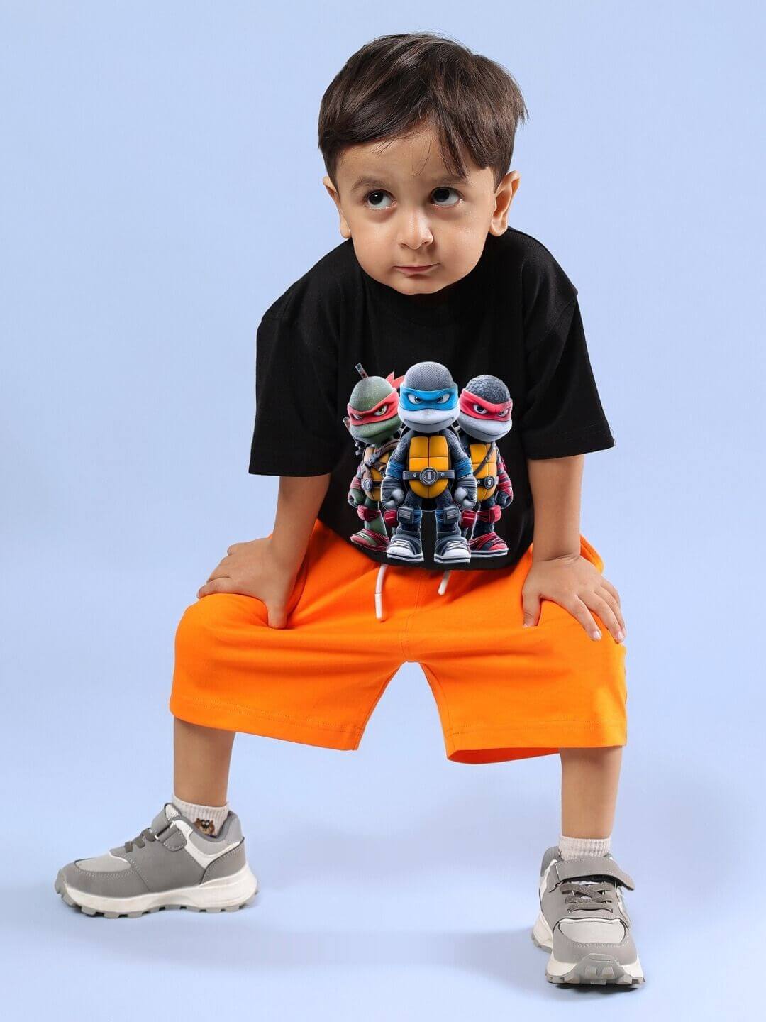 Child wearing Ninja Turtles black T-shirt and orange shorts set, showcasing playful superhero design for boys and girls.