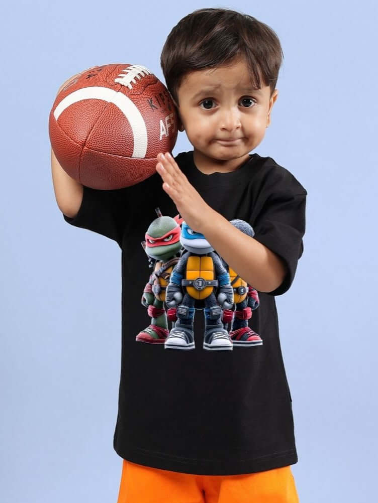 Child wearing NINJA TURTLES T-SHIRT FOR BOYS AND GIRLS BLACK holding a football