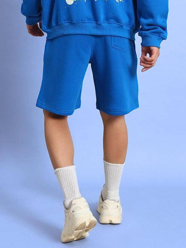 Back view of person wearing NO DRAMA COTTON FLEECE SHORTS ROYAL BLUE showcasing casual streetwear style with elastic waistband and pockets.