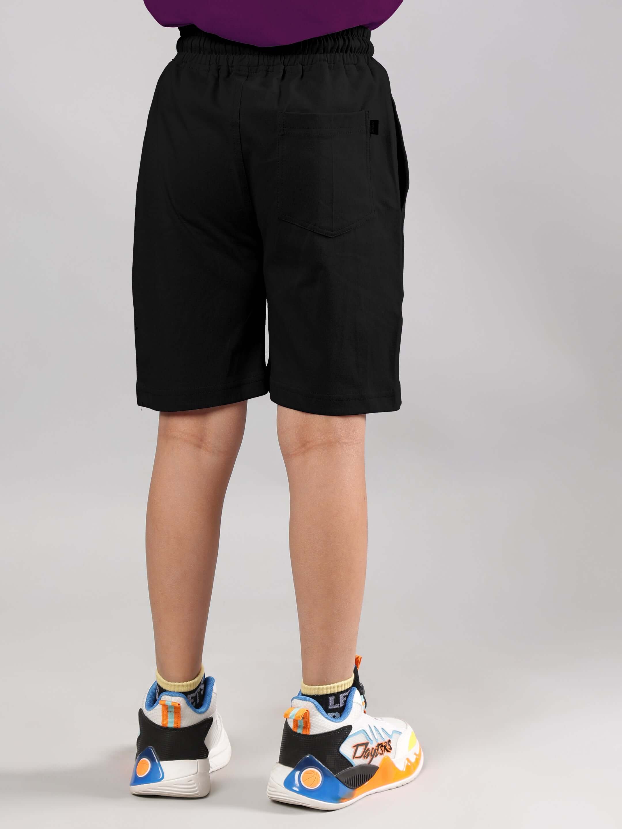 Child wearing NO POS WOW purple-black co-ord shorts set, sneakers visible, back view. Unisex design by DUDS.