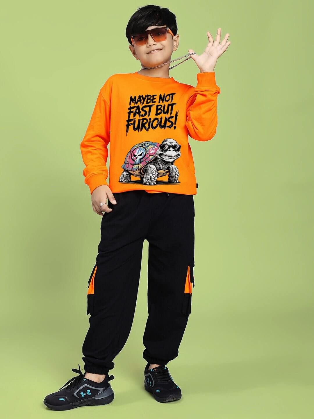 Child wearing NOT FAST BUT FURIOUS PRINT SWEATSHIRT BOYS AND GIRLS ORANGE with turtle graphic, posing in stylish outfit.