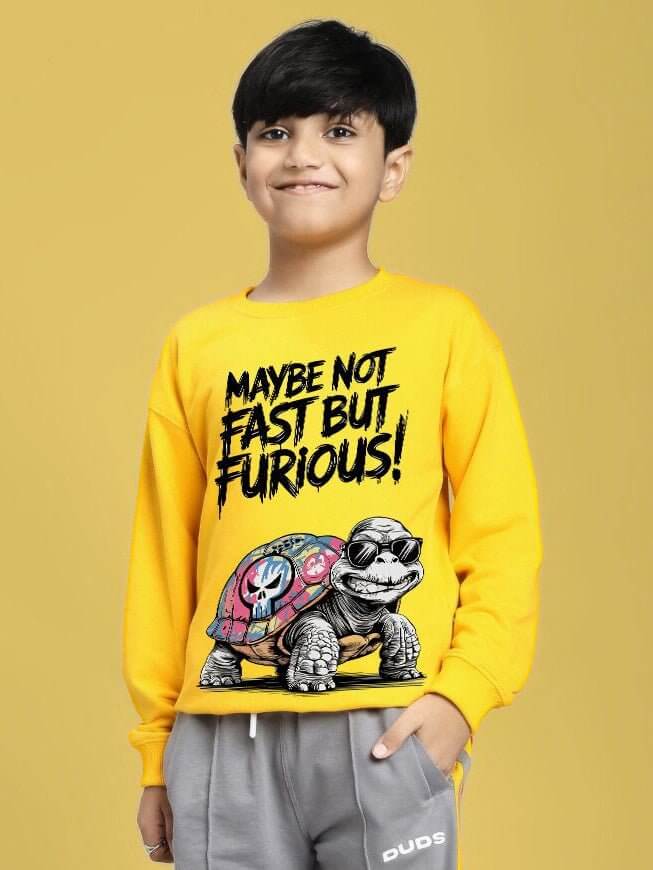 Child wearing NOT FAST BUT FURIOUS PRINT SWEATSHIRT BOYS AND GIRLS YELLOW with turtle graphic on front, smiling, yellow background.