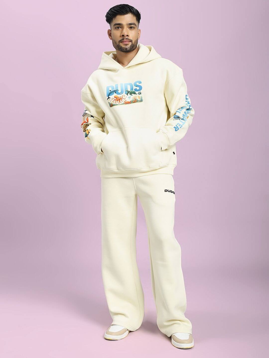 Model wearing OCEAN BUDDIES FLEECE CO-ORD SET OFF-WHITE with sea-inspired graphics on a pink background