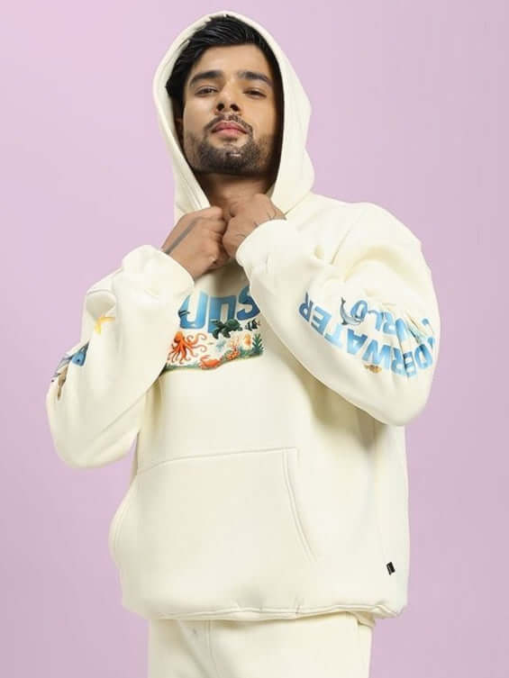 Man wearing OCEAN BUDDIES OVERSIZED FLEECE HOODIE OFF-WHITE with ocean-themed graphics on sleeves