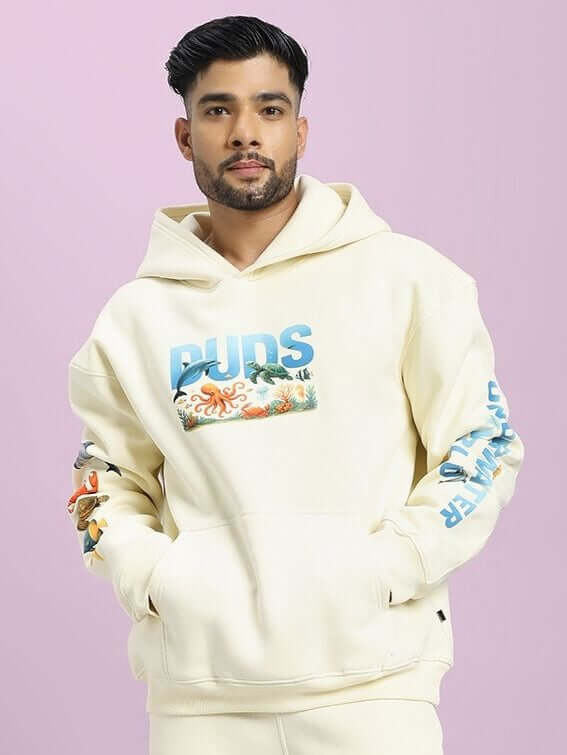Man wearing OCEAN BUDDIES OVERSIZED FLEECE HOODIE OFF-WHITE with whimsical ocean design, showcasing relaxed and cozy fit.