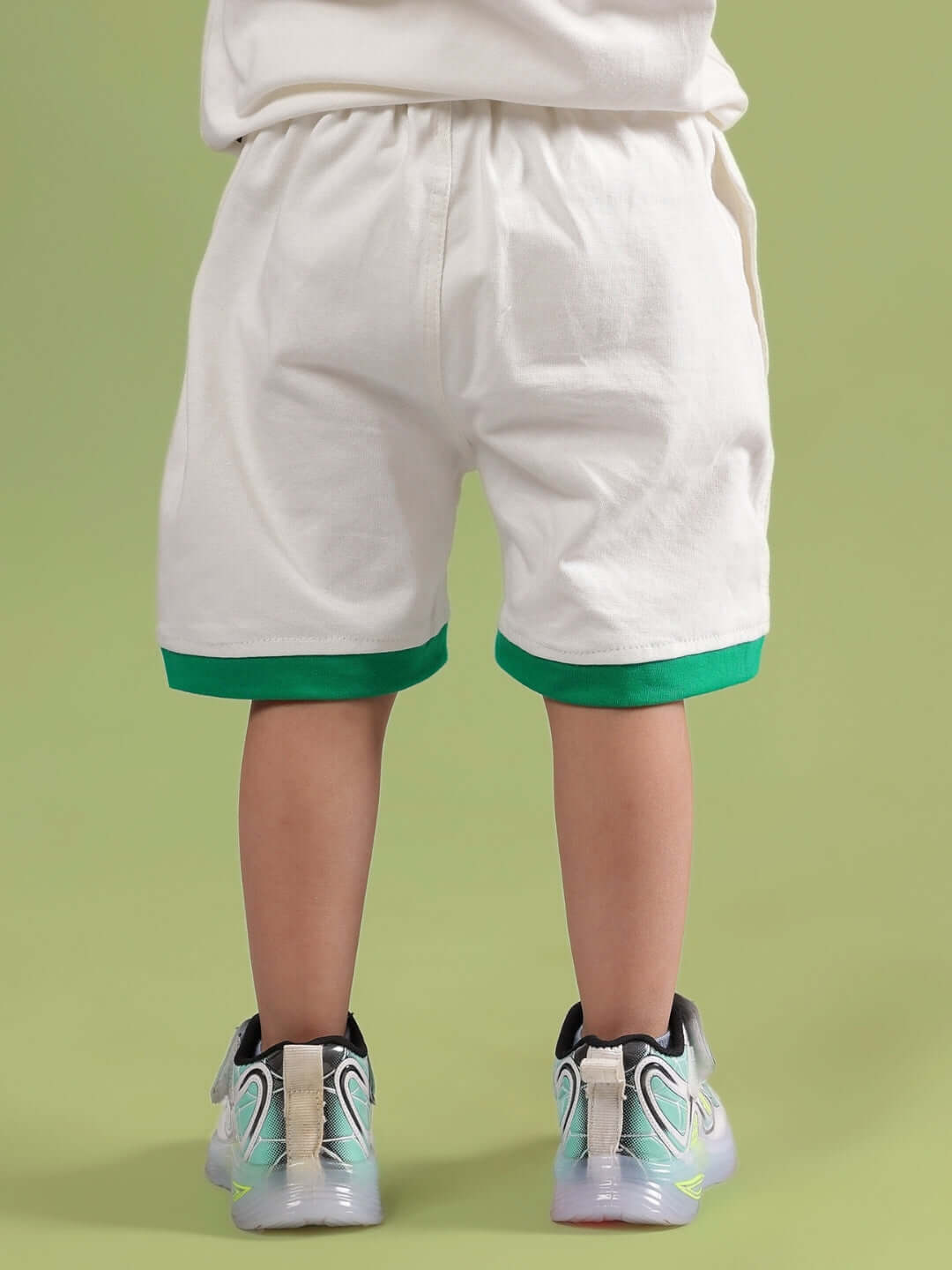Child wearing DRIBBLE SHORTS FOR BOYS & GIRLS OFF WHITE with green trim, viewed from the back.