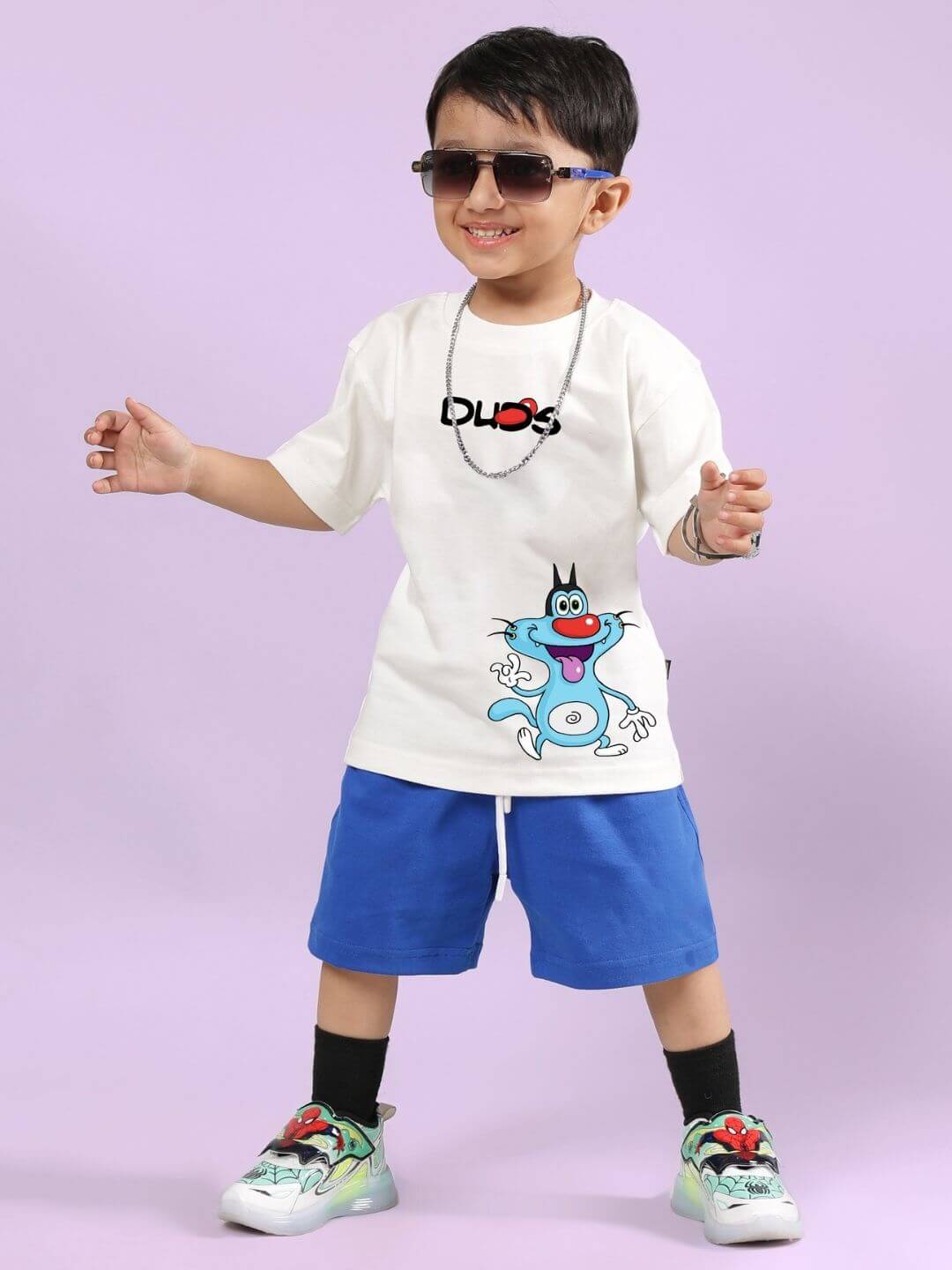 Kid wearing an Oggy Printed Co-Ord Set with off-white T-shirt and blue shorts, featuring cartoon print, standing against a purple background.