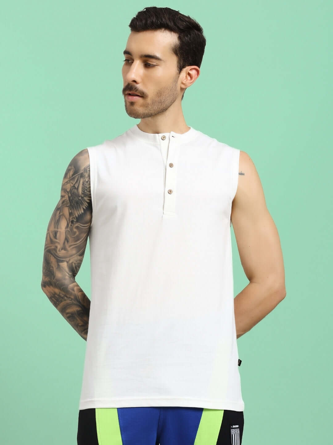 Man wearing OLIN REGULAR FIT T-SHIRT OFF-WHITE, showcasing sleeveless design and tattoos, against green background.