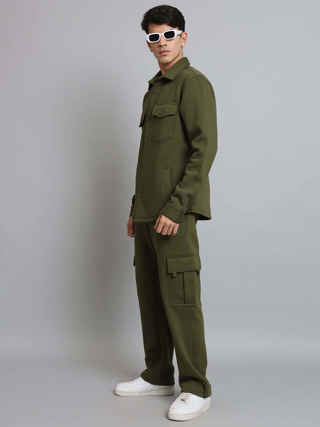Model wearing olive green relaxed fit fleece cargo pants with white sneakers against a gray background.