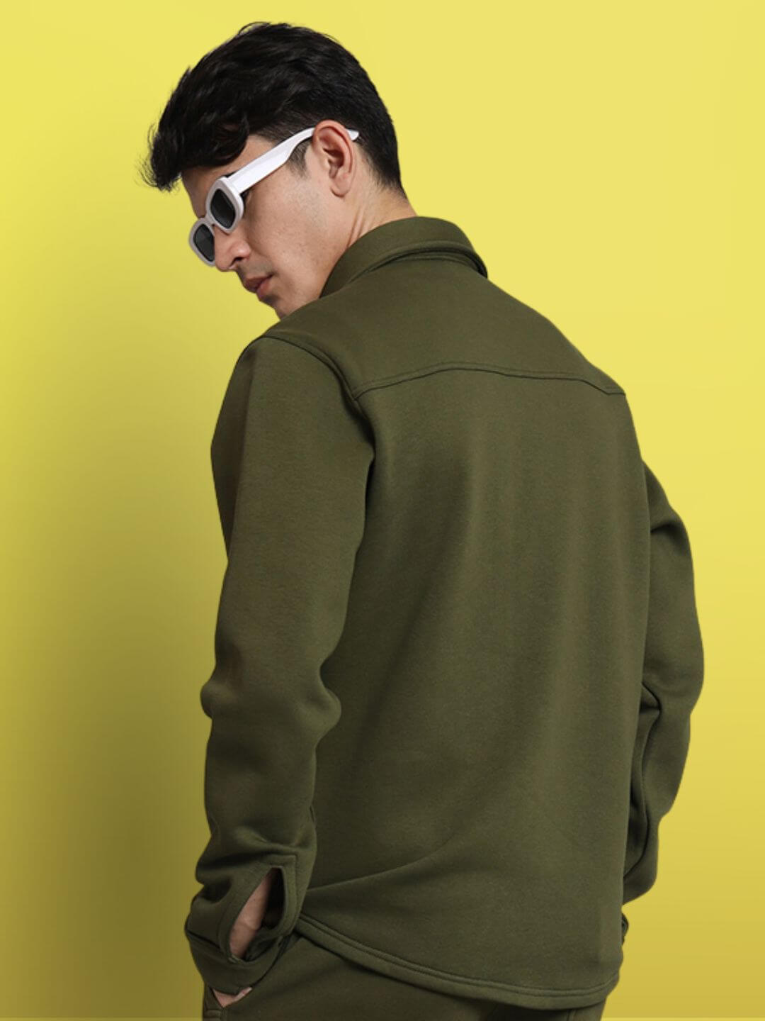 Back view of model wearing olive green relaxed fit full sleeves fleece overshirt against a yellow background, stylish and comfortable.