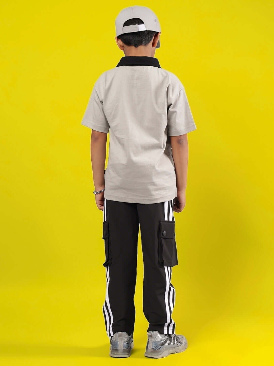 Child wearing ORION CO-ORD FOR BOYS & GIRLS GREY-BLACK outfit, showcasing back design with a hat on a vibrant yellow background.
