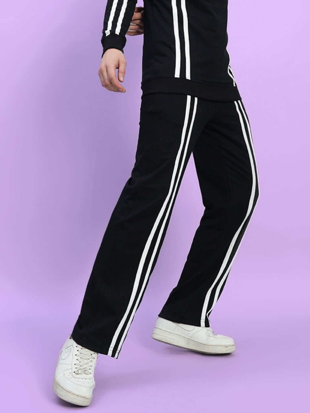 Person wearing black joggers with two white stripes, standing on a purple background.