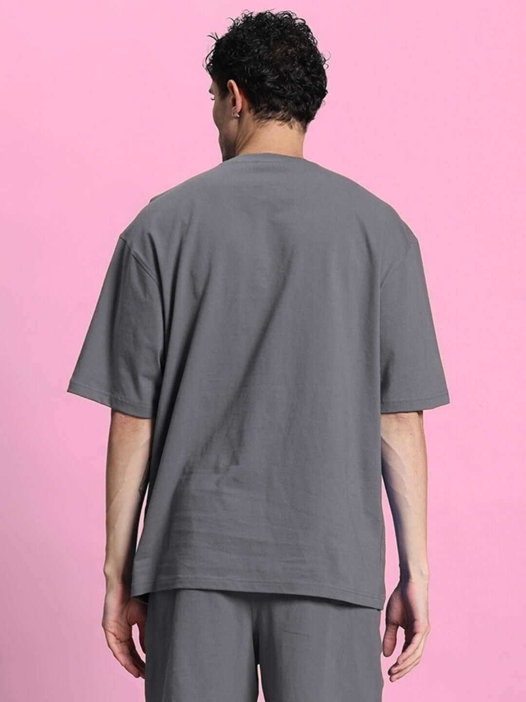 Back view of OUTLOOK OVER-SIZED T-SHIRT GREY on model, showcasing a relaxed fit and minimal style against a pink background.