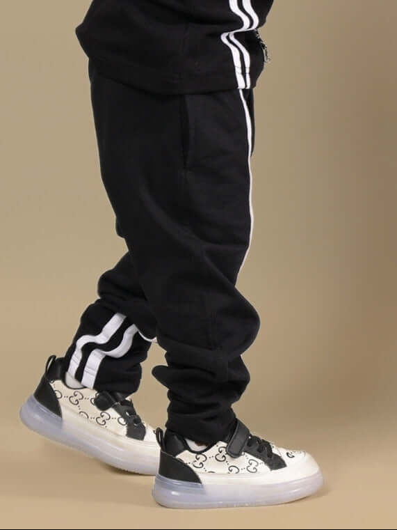 OUTLOOK JOGGER FOR BOYS GIRLS BLACK with white stripe detail, shown on a child wearing patterned sneakers.
