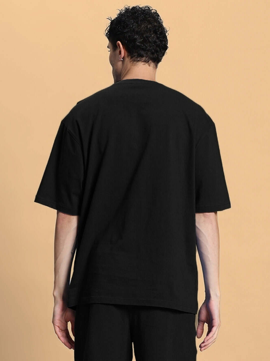 Rear view of person wearing OUTLOOK OVER-SIZED T-SHIRT BLACK, showcasing relaxed fit and premium fabric quality.
