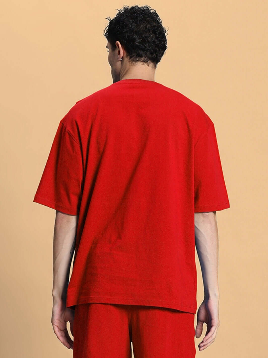 Man wearing OUTLOOK OVER-SIZED T-SHIRT RED, showcasing back view of bold-colored comfortable fit tee against neutral background.