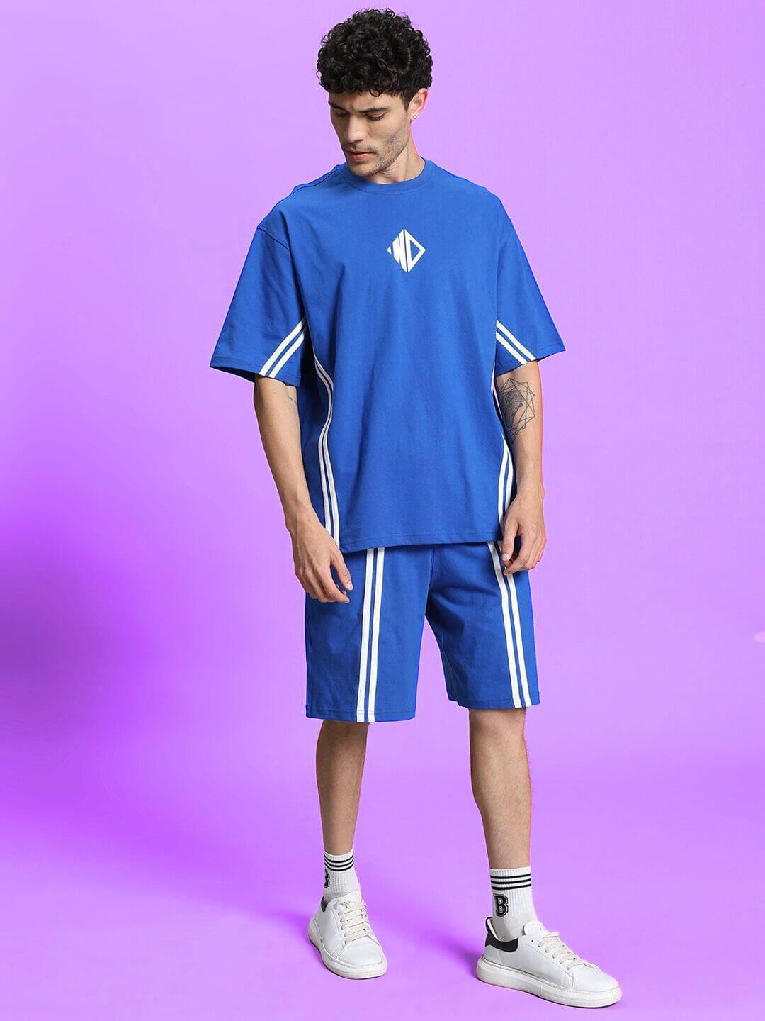 Man wearing blue summer co-ord shorts set with white stripes, featuring premium cotton fabric and casual style, on a purple background.