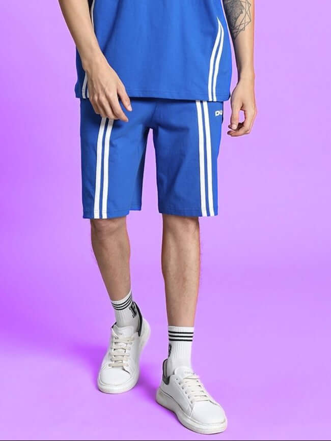 OUTLOOK REGULAR FIT SHORTS ROYAL BLUE worn with white sneakers, showcasing vibrant hue and comfortable fit against a purple background.