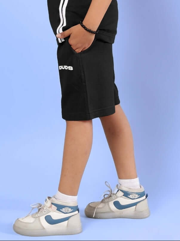 Child wearing OUTLOOK SHORTS FOR BOYS GIRLS BLACK with sneakers, showcasing sporty style and comfort on a light blue background.