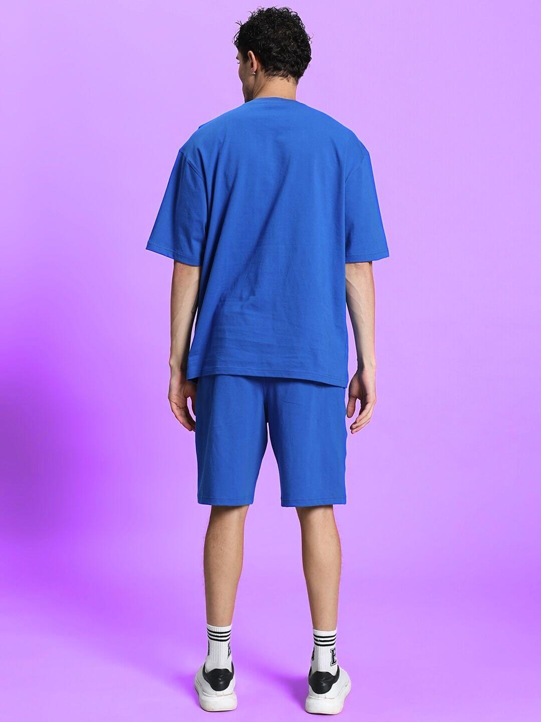 Man wearing blue co-ord shorts set, showcasing premium cotton fabric, suitable for summer fashion. Back view against a purple background.