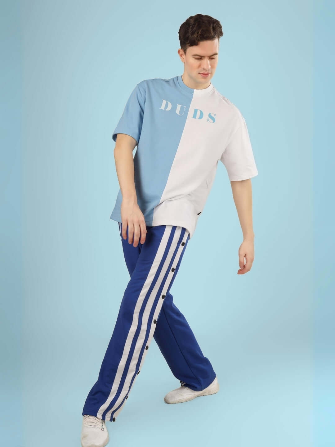 Model wearing G.O.A.T oversized T-shirt in sky blue-white, premium cotton with elastane, styled with blue striped pants.