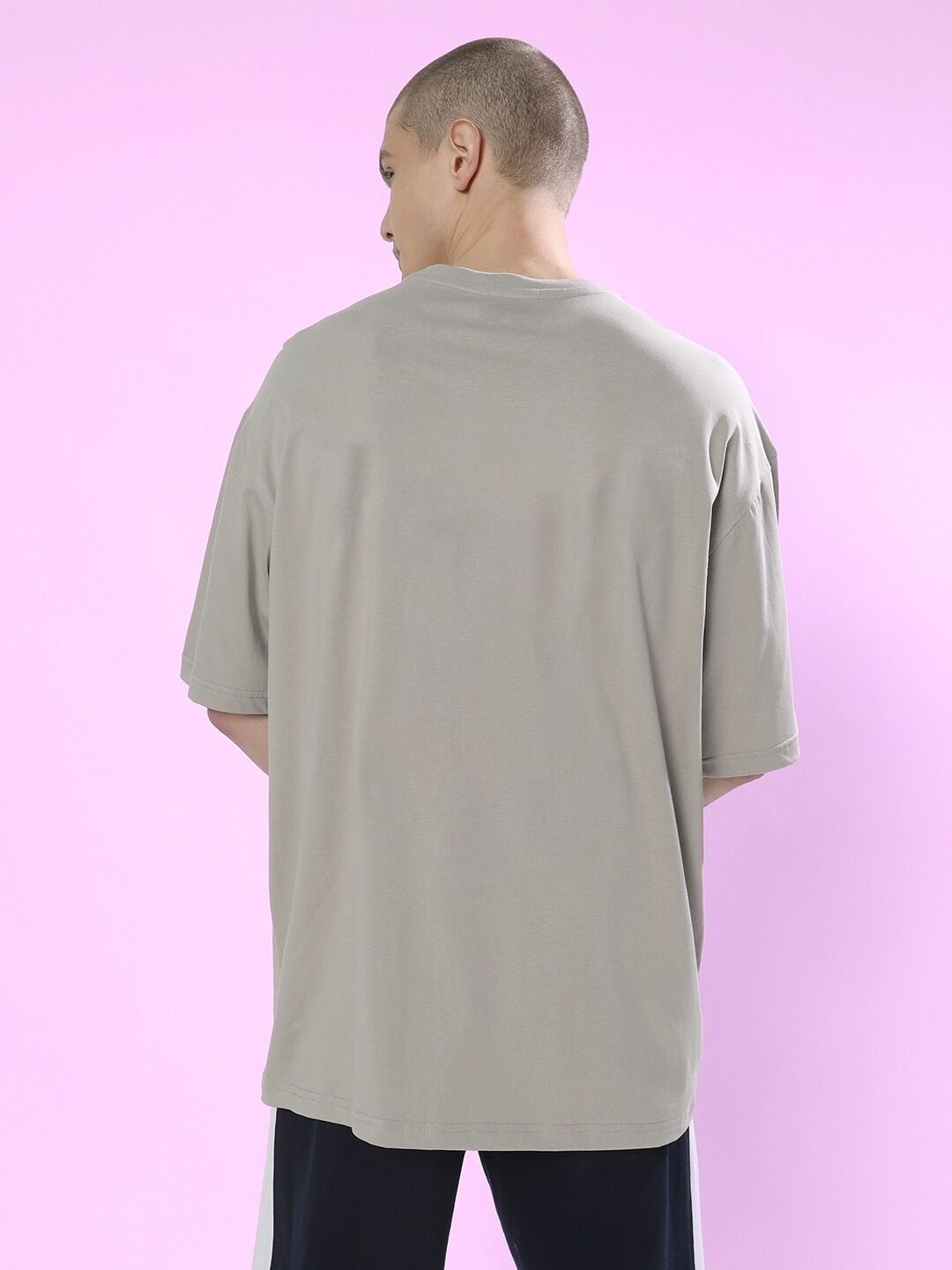 Back view of person wearing ANXIETY OVER-SIZED T-SHIRT GREY against a pink background.
