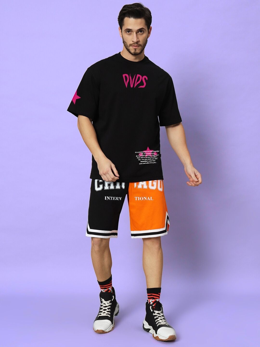 Model wearing MODERN LOVE OVER-SIZED T-SHIRT BLACK with colorful shorts on a purple background.