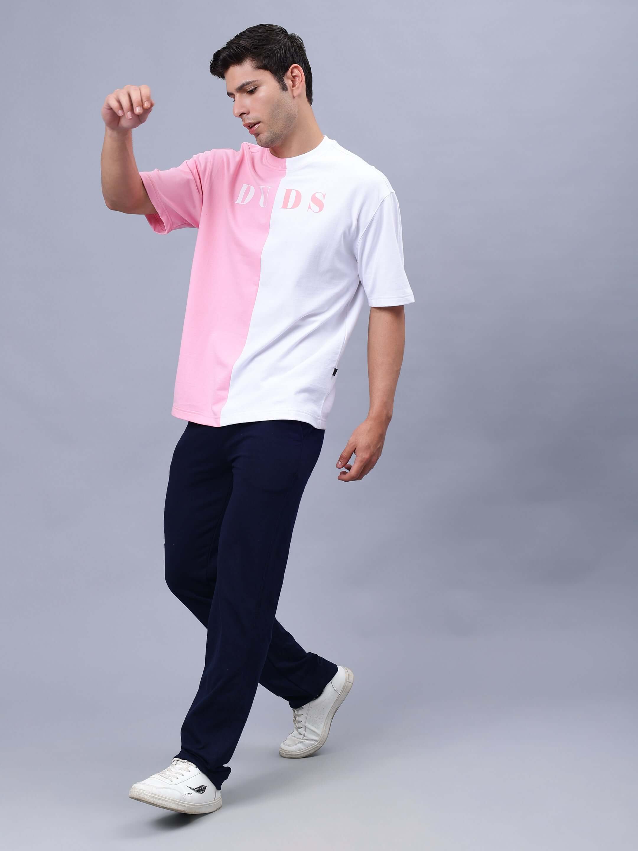 Model wearing G.O.A.T oversized T-shirt in pink and white, made of premium cotton fabric, styled with dark pants, showcasing casual fashion.