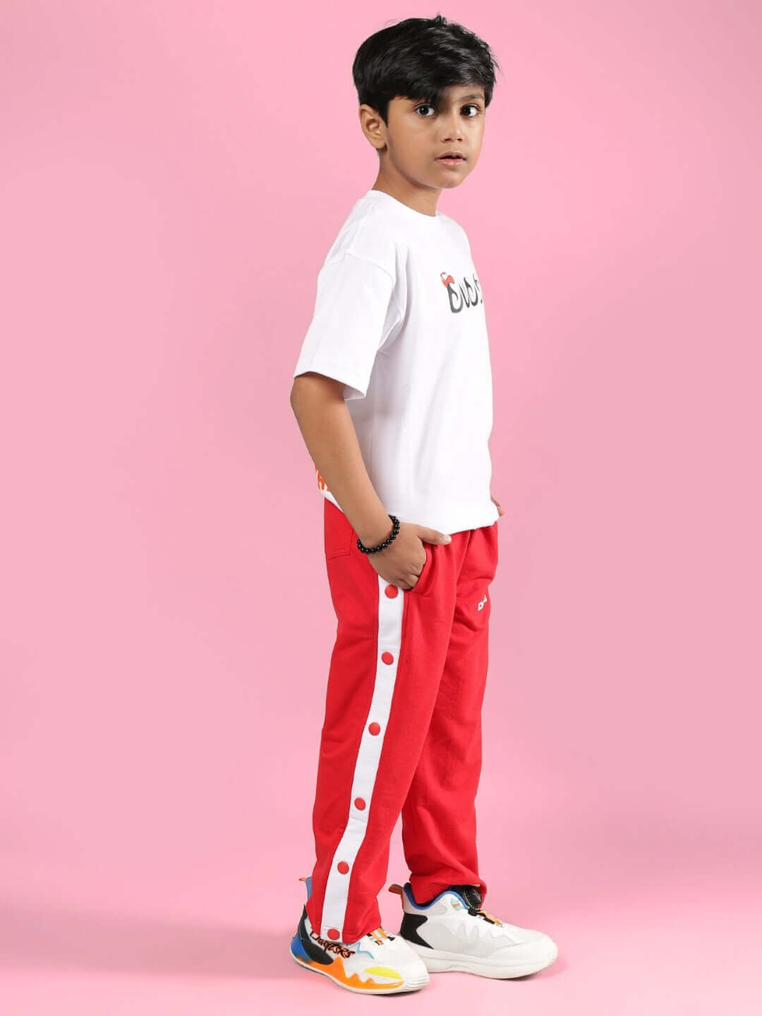 Child wearing PALOMA CO-ORD FOR BOYS & GIRLS WHITE RED, showcasing stylish white top and red pants against a pink background.