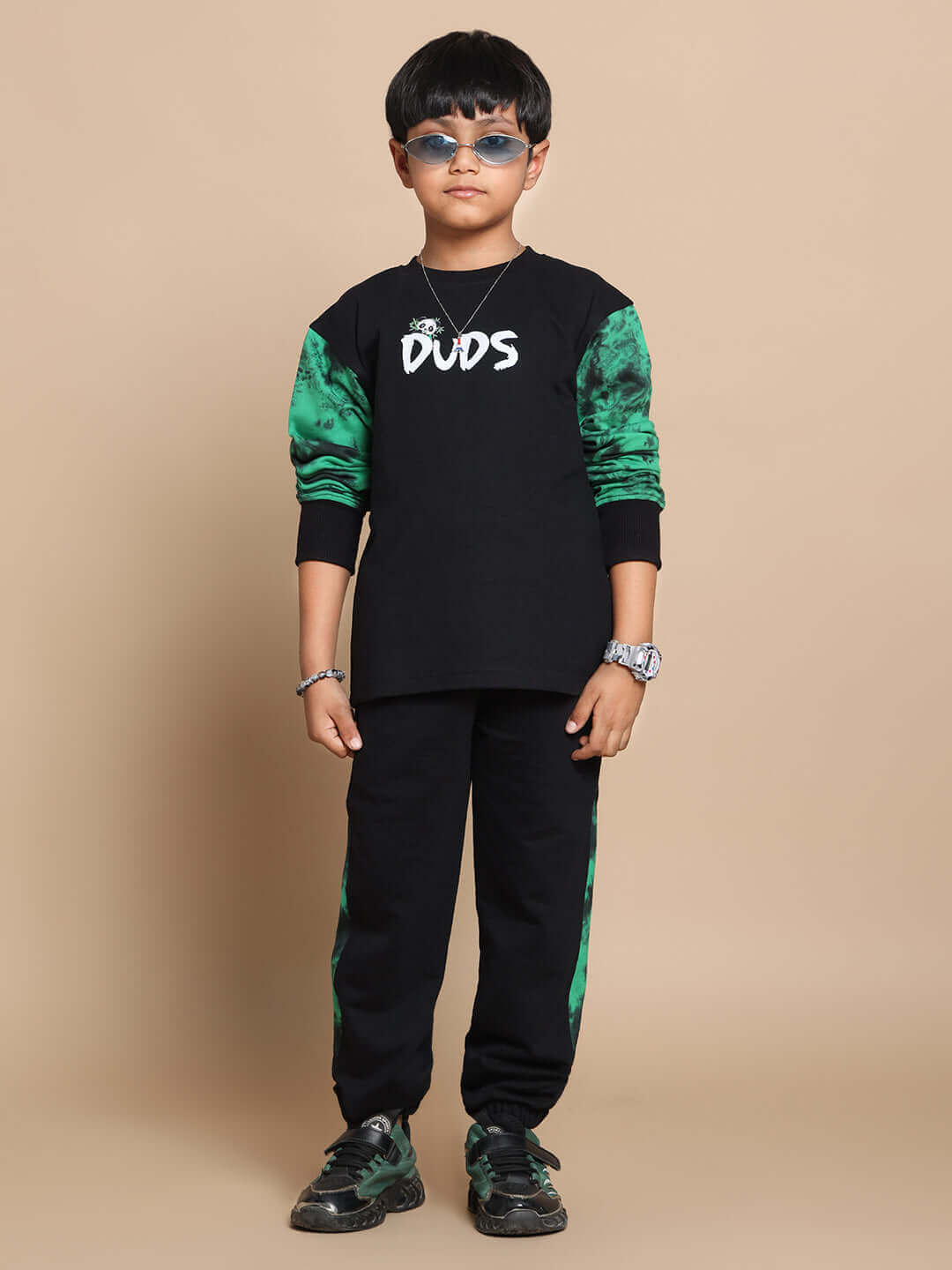 Young boy wearing a black DUDS panda co-ord set with green sleeves, sunglasses, and sneakers, showcasing fashionable kidswear.