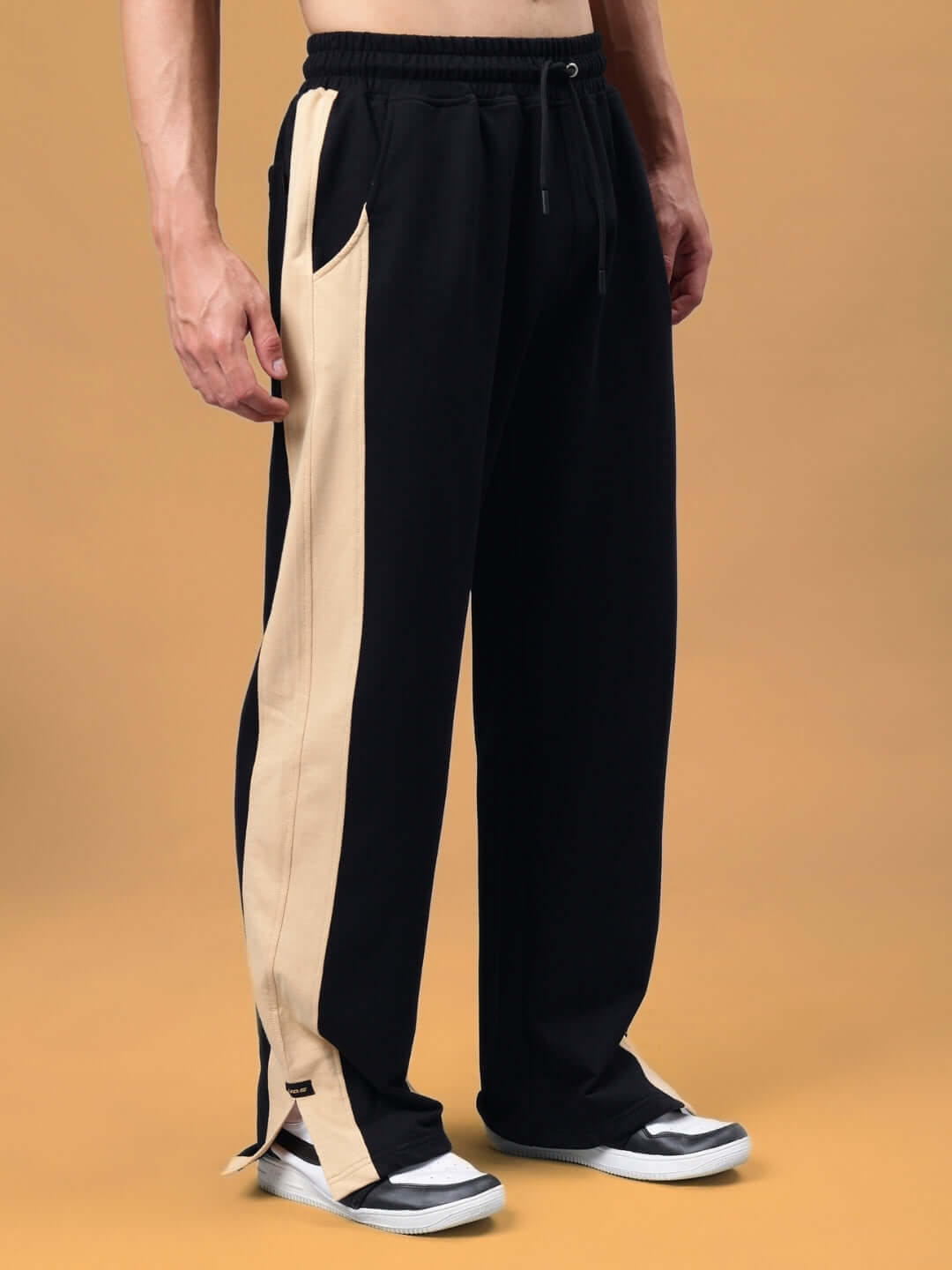 Man wearing Paradise Side Slit Joggers in black-beige with elastic waistband and side pockets, made by DUDS, on a neutral background.