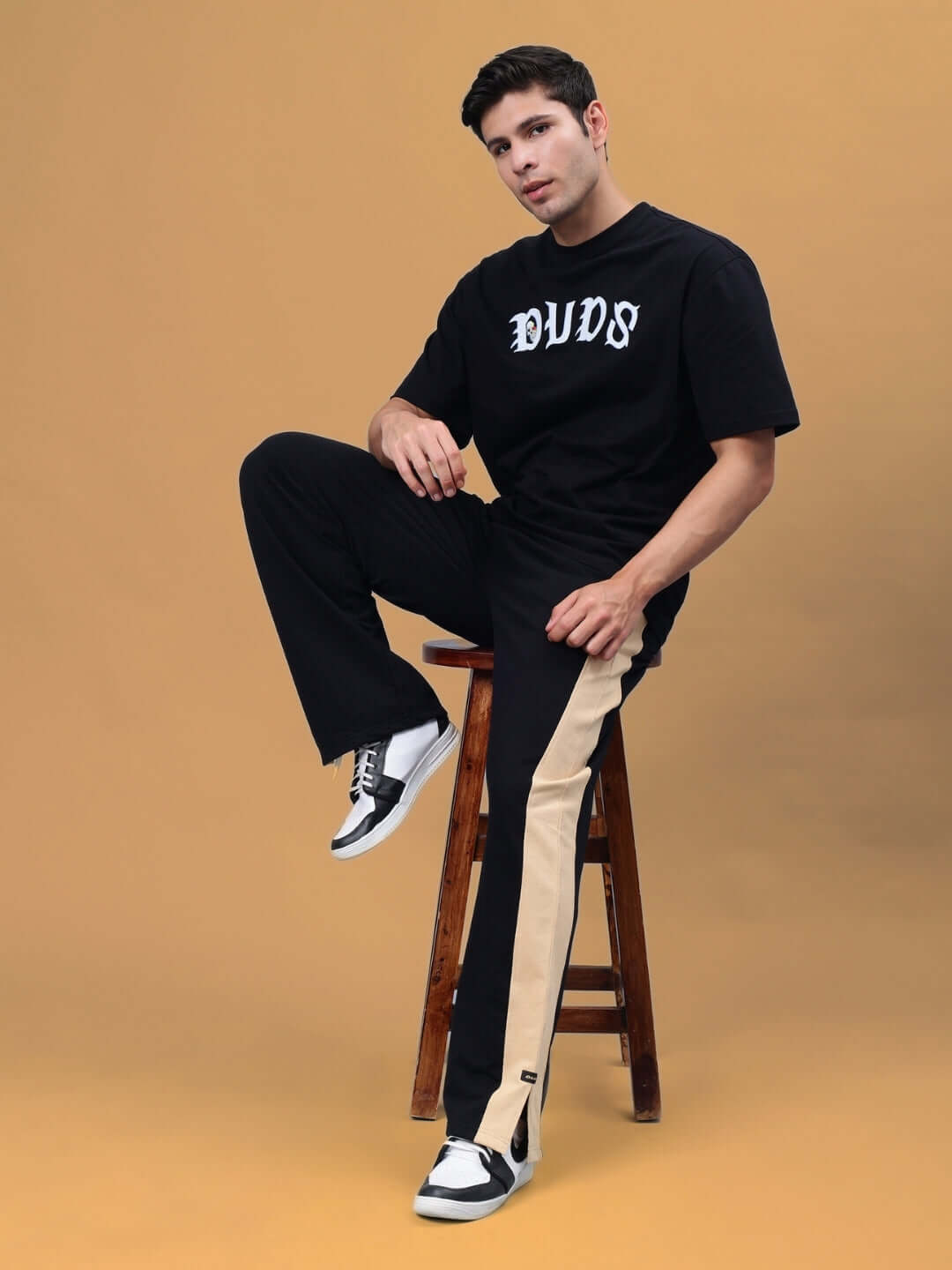 Model wearing Paradise Side Slit Joggers in black and beige by DUDS, showcasing a stylish, made-to-order design with a slit detail.