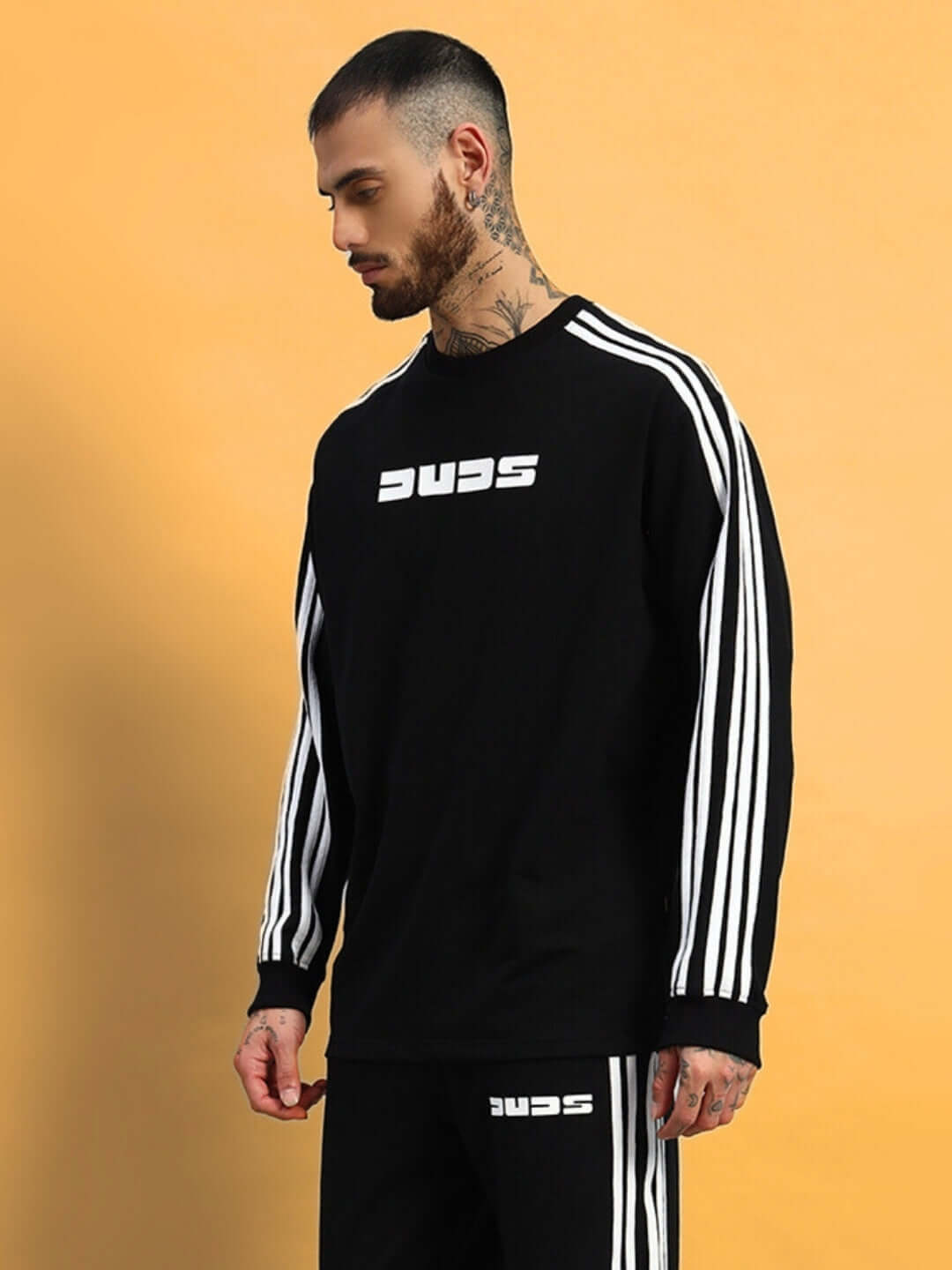 PARKA oversized black sweatshirt with white stripes, made of premium cotton French terry, worn by tattooed model against yellow background.
