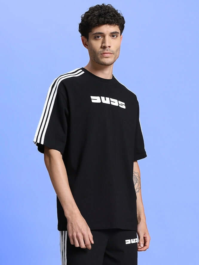 Man wearing PARKA OVER-SIZED CLASSIC T-SHIRT BLACK against blue background, showing relaxed fit and premium cotton fabric.