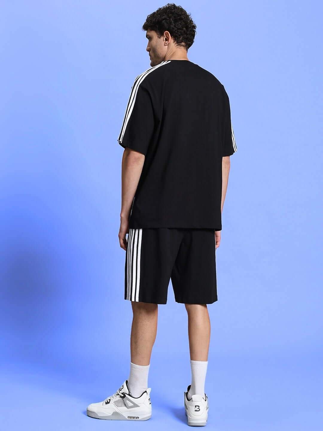 Man wearing PARKA REGULAR FIT SHORTS BLACK with casual sneakers against a blue background, showcasing stylish, breathable design.